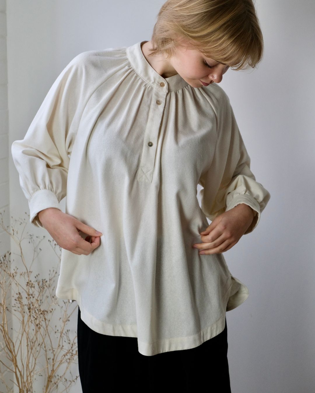 woman standing against white background wearing a white shirt.