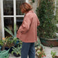 Woman standing in conservatory wearing pink jacket.