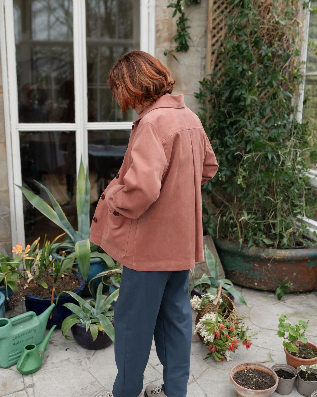 Woman standing in conservatory wearing pink jacket.