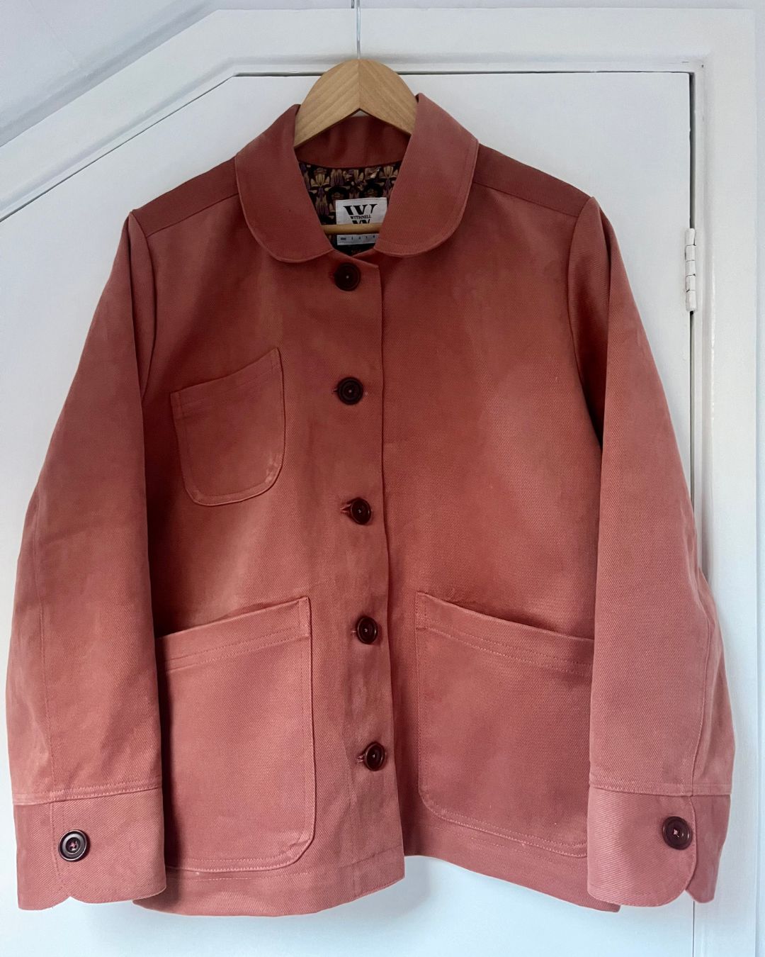 pink jacket on a wooden hanger against white background.