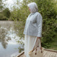 Woman standing on a wooden platform by a body of water, holding a woven bag.