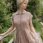 Woman wearing a checkered dress standing outdoors with greenery in the background