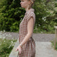 Woman in a checkered dress standing outdoors with greenery in the background