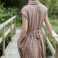 Woman in a checkered dress standing on a wooden bridge in a natural setting